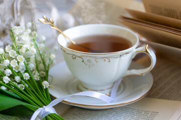 A cup of tea, coffee, a bouquet of lilies of the valley, an old book.