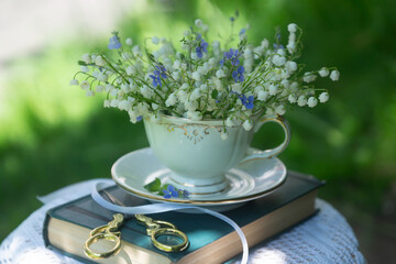 A cup of tea, coffee, a bouquet of lilies of the valley, an old book.