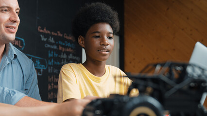 African boy using laptop to program code or prompt with car model placed while teacher and...