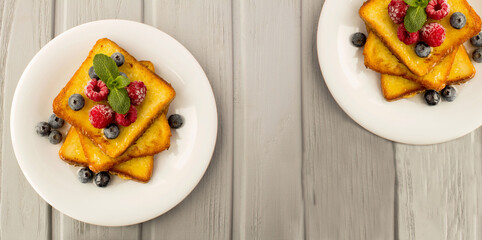 French toasts with berries and honey in the white plate on the gray wooden background. Top view. Copy space.