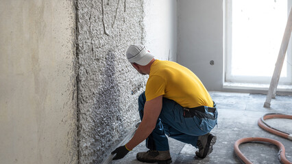 Machine plastering. Applying gypsum plaster by mechanized method on a wall. A worker hand removes excess plaster with leveler.