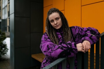 Lifestyle concept. A young woman with dreadlocks and piercings stands at the entrance to an orange house