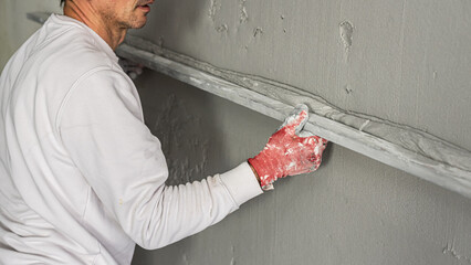 Machine plastering. Applying gypsum plaster by mechanized method on a wall. A worker hand removes...
