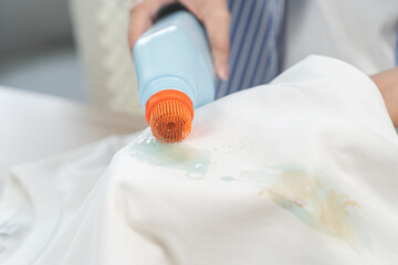 Dirty stain concept, asian young housewife woman removing spill from white T-shirt hand holding stain remover bleach bottle to remove dirt stain, stains on clothes, dirty spot for washing and cleaning