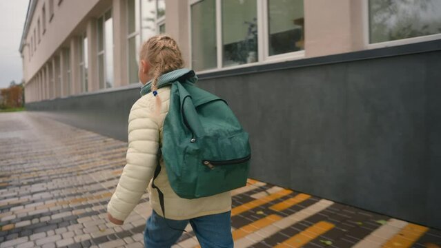 Back view girl running street outside city jogging schoolgirl with backpack fast little female school after lessons educational day kid pupil childish amusement vacations hurry playful motion activity