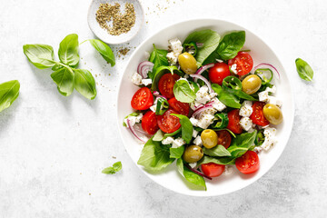 Fresh healthy vegetable Mediterranean salad of feta cheese, tomato, olives, green pepper and green basil leaves, top view