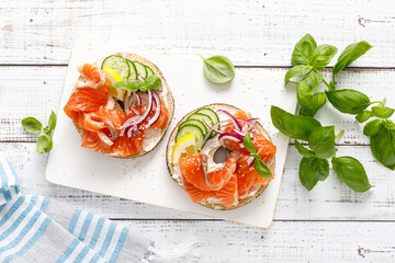 Salmon sandwiches with bagel, salted fish, fresh cucmber, onion and basil on white background, top...