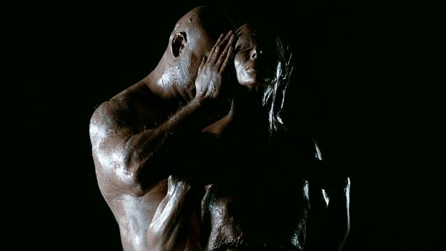 In the black void, a man with a strong physique and his clay-covered wife demonstrate their unbreakable bond and devotion.
