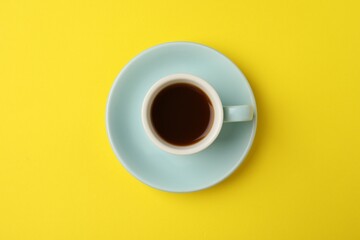 Tasty coffee in cup on yellow background, top view
