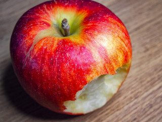 Half-Eaten Apple. A vibrant red apple, partially eaten, against a wooden backdrop, suitable for nutrition and diet content.