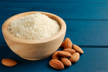 Fresh almond flour in bowl and nuts on blue wooden table, closeup. Space for text