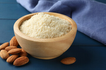 Fresh almond flour in bowl and nuts on blue wooden table, closeup