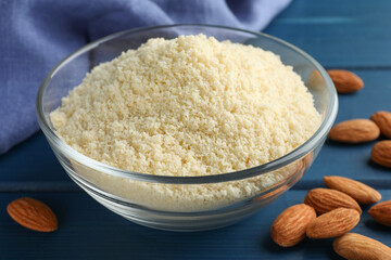 Fresh almond flour in bowl and nuts on blue wooden table, closeup