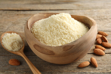 Fresh almond flour in bowl, spoon and nuts on wooden table, closeup
