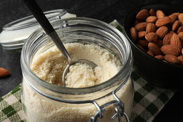 Fresh almond flour in jar and nuts on dark table, closeup