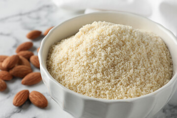 Fresh almond flour in bowl and nuts on light table, closeup