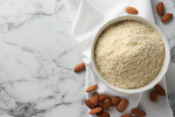 Fresh almond flour in bowl and nuts on white marble table, top view. Space for text