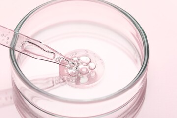 Glass pipette and petri dish with liquid on pink background, closeup