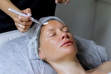 Middle aged female receiving facial anti aged massage in beauty salon. Skincare concept. Cosmetology specialist making facial lifting massage, appling cosmetic product to facial skin with brush