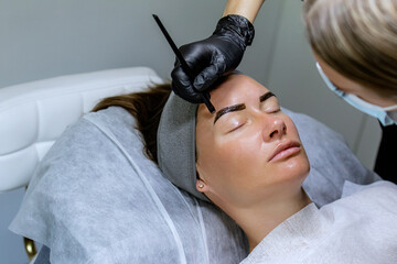 The makeup artist, cosmetology specialist performing long-term eyebrow styling and paints the...