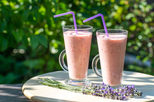 Glass of fresh strawberry milkshake, smoothie and fresh strawberries in garden on wooden table and green background. Healthy food and drink concept.