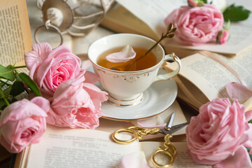 A cup of aromatic tea, a book and a rose on the table.