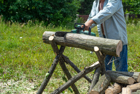 A man is sawing a tree with a chainsaw. A young near his house