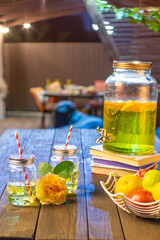 drink station with small bottles and homemade lemonade on wooden terrace with abstract night light bokeh of night festival in garden, copy space for display of product or object presentation