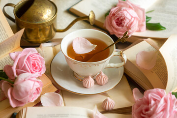 A cup of aromatic tea, a book and a rose on the table.