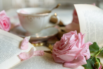 A cup of aromatic tea, a book and a rose on the table.