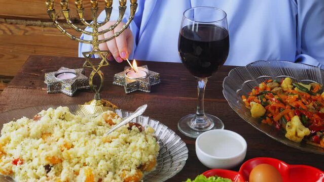 The hand of a Jewish woman lights candles on the Passover Seder holiday at a laid table. Medium plan