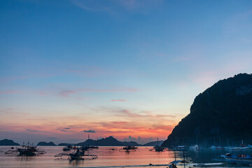 Traditional Filipino banca boats with outriggers anchored off the beach at sunset in tropical...