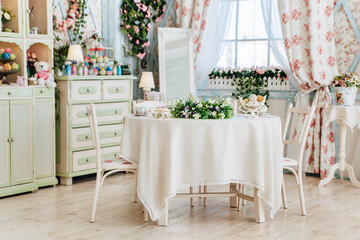 Cozy vintage dining room, floral design, pastel green and white furniture, flower arrangements on table, large window, decorative elements, inviting atmosphere, light-filled space
