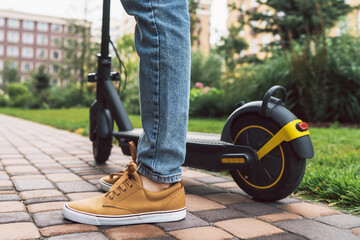 Low angle view of male legs standing near electro scooter at the street