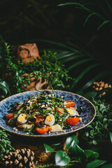 A fresh greeA close-up shoot of a salad with cherry tomatoes, eggs, and olives on a blue plate, surrounded by lush green foliage.n salad with cherry tomatoes, eggs, and olives served on blue plate