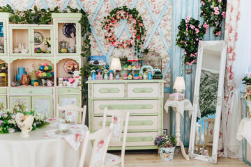 Charming kitchen or living room with vintage decor, pastel colors, floral wreath, large mirror, shelves filled with decorations, inviting atmosphere, soft lighting, wooden floor. Focus on background