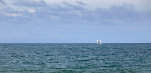Obraz premium Sailboat sailing through the Atlantic Ocean near the coast, next to the horizon, on a summer day