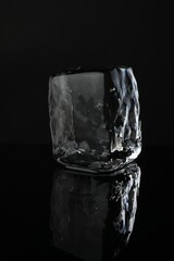 One cube of clear ice on black mirror surface