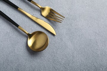 Stylish golden cutlery on grey table, above view. Space for text