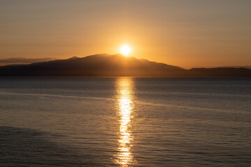 The sun sets behind the mountain on the opposite coast of the sea