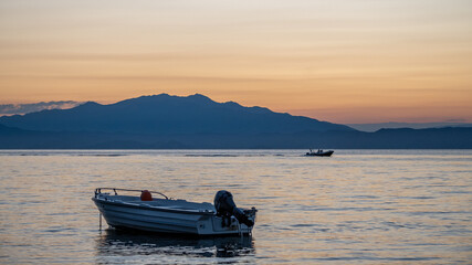 A boat floats on the sea at sunset while another boat sails on the horizon