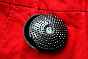 Broken anti-theft tag with drill bit on red fabric, anti theft device used in clothes store, tag on...