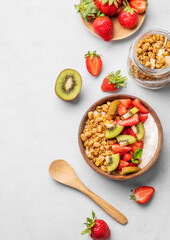 Natural yogurt with granola, kiwi and strawberries in a wooden bowl on a light background with fresh berries and fruits.