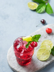 Cherry-lime mojito cocktail with mint, lime and ice on a marble board on a light  background.