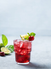 Cherry-lime mojito cocktail with mint, lime and ice on a blue background.