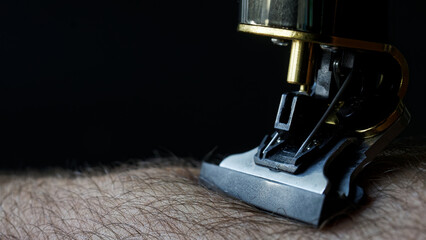 Shaving head of a modern professional trimmer on a hairy area of ​​the body. Hygiene and safe shaving concept. Dark background. Photo. Selective focus