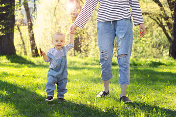 Fototapeta premium baby walks holding mother's hand, baby's first steps