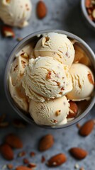 Overhead view of a bowl filled with light beige ice cream topped with almonds in a grey pot.
