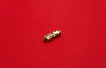 Transparent capsule filled with golden heart confetti on red background. Love pill concept. Selective focus, copy space