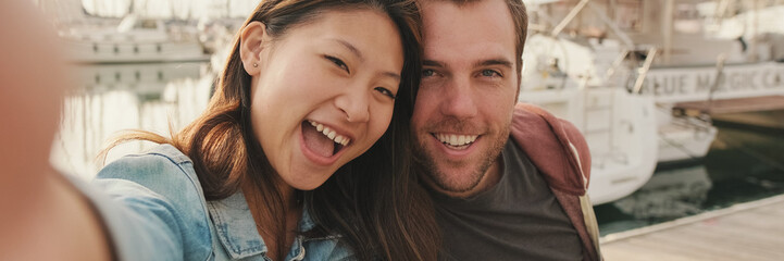 Romantic couple sits on the pier on the yacht background and take a selfie, panorama